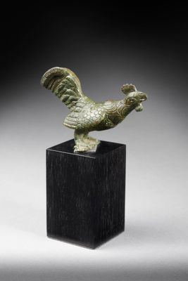 une figurine en bronze représentant un coq, posée sur un socle noir