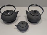three black teapots sitting on a white table with a white background