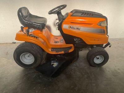 une tondeuse à gazon orange sur laquelle on peut monter, garée dans un garage