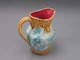 un vase bleu et jaune avec une anse rouge sur un fond gris