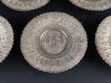 four silver plates with designs on them sitting on a black surface