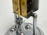 a silver clock that is on a stand on a white surface