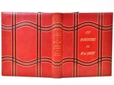 an old book with a red cover sitting on top of a white table