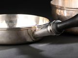 un bol en argent et une poêle en argent posés sur une table noire