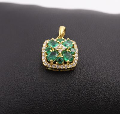 an emerald and diamond pendant on a black leather surface