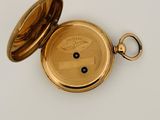 a gold pocket watch on a white surface with a key