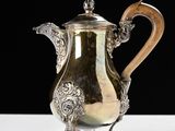 an antique silver coffee pot with a wooden handle on a white table
