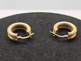 une paire de boucles d'oreilles créoles en or posées sur une surface noire