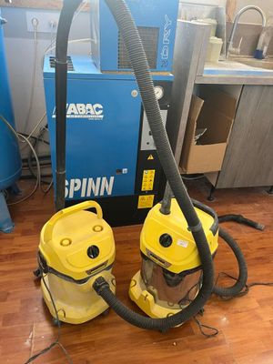 two yellow vacuums sitting on a wooden floor next to a blue machine