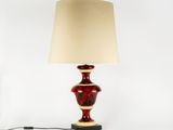 a red table lamp with a beige shade on top of it