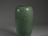 a green vase sitting on top of a table next to a gray wall