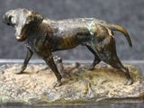 bronze statue of a dog standing on a rock with a black background
