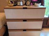 a white dresser with three drawers and a clock on top of it