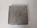 a small metal box with a piece of gold in it