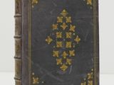 an old book with gold and black cover sitting on a white surface