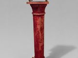 une horloge rouge posée sur un socle, sur fond gris