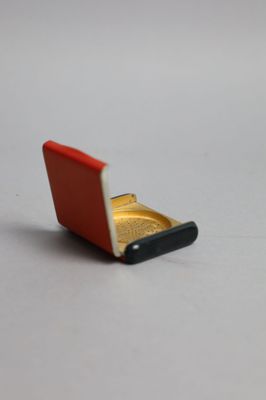 un petit étui à cigarettes rouge et doré posé sur une surface blanche