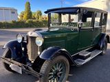 an old green car parked in a parking lot next to a building