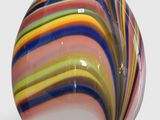brightly colored glass egg sitting on a metal stand on a white surface