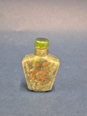 yellow jade snuff bottle with chinese writing on it on a blue surface