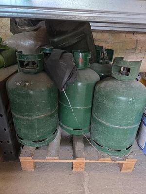 Plusieurs bouteilles de gaz vert sont empilées sur une palette dans un garage.