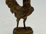 statue d'un coq posée sur un socle en bois, sur une surface blanche