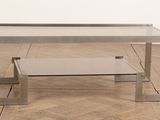 une table basse en verre avec un piètement en métal, posée sur un parquet