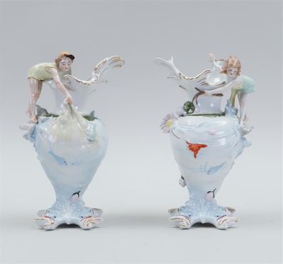 pair of porcelain vases with figures on top of them