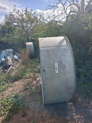 a trash can sitting on the side of the road next to a bush