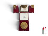 a gold medal sitting in a red box on a white surface