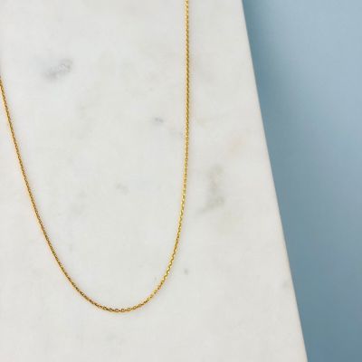 un collier à chaîne en or posé sur une dalle de marbre