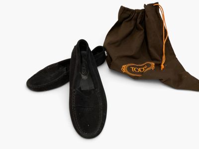 une paire de pantoufles en daim noir et un sac fourre-tout posés sur une surface blanche