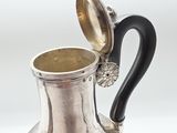 an antique silver pitcher with a black handle on a white background
