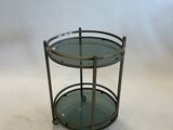 une table ronde en verre avec un piètement en métal et deux étagères