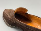 une personne porte des mocassins marron sur une surface blanche