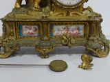 a gold clock sitting on top of a table next to a miniature figurine