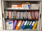many folders and binders on a shelf in a cabinet