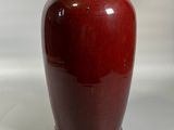 un vase rouge posé sur une surface blanche