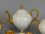 a white and gold tea set with gold cups and saucers
