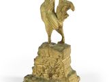 statue en or représentant un coq posé sur un rocher, sur fond blanc