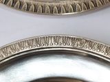 two silver plates with designs on them on a table