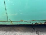 rust on the side of a green car on a street