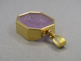 une image représentant un pendentif doré et violet orné d'une pièce de monnaie