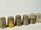 six dés à coudre anciens alignés sur une surface blanche