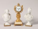 three statues and a clock on display on a table