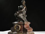 bronze statue of a woman sitting on a table with a clock in front of her
