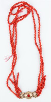 un collier de perles rouges muni d'un fermoir en argent, sur fond blanc