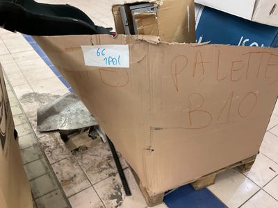 une boîte en carton sur laquelle est accrochée une pancarte, posée par terre