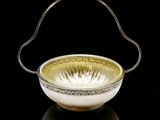 a gold and white bowl with a handle on a black surface
