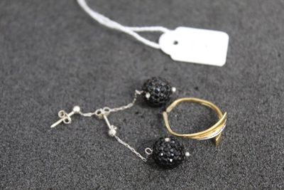 une paire de boucles d'oreilles noires et dorées et une bague dorée posées sur une surface grise